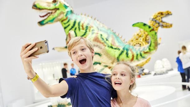 Geschwister machen ein Selfie vor den LEGO Dinosauriern im LEGO House in Billund
