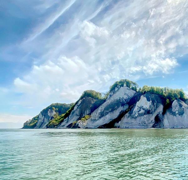 Das Bild zeigt einen blauen Himmel, türkisfarbenes Meer und die Klippen von Møn. 